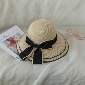 Elegant beige straw beach hat with a large black bow, styled with a magazine and glasses