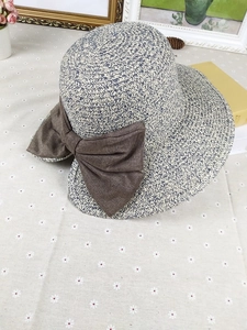 Detail of wide brim straw sun hat featuring a mixed-weave texture and a large brown bow
