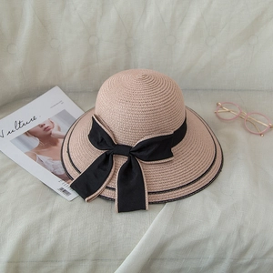 Detail of a beige woven sun hat featuring a wide brim and a large black ribbon bow