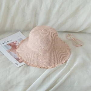 Pink woven straw sun hat with frayed edge detail on white fabric background