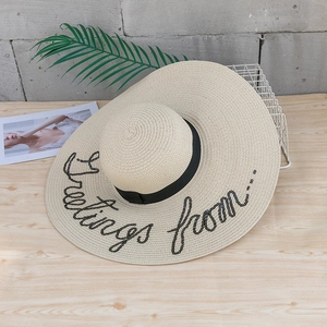 Détail d'un chapeau de paille à large bord avec broderie pailletée et ruban sur bois