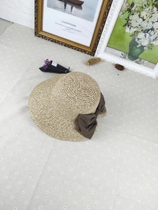 Detail of handwoven straw sun hat featuring a large elegant brown fabric bow accent