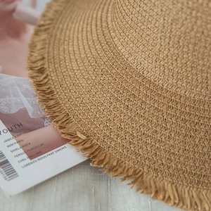 Close-up of the fine woven texture and raw fringe edge of the khaki straw sun hat