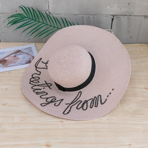 Détail du chapeau de paille avec ruban noir et lettrage Greetings en paillettes