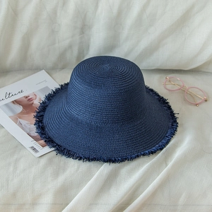 Navy blue foldable straw sun hat with frayed fringe edges on a white fabric background