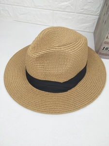 Detail of khaki straw fedora hat featuring woven texture and black fabric ribbon band