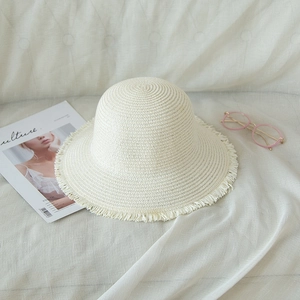 Foldable beige straw hat with floral fringe brim and magazine on soft fabric background