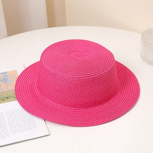 Detail of pink straw boater hat showing fine woven texture on a minimalist white table