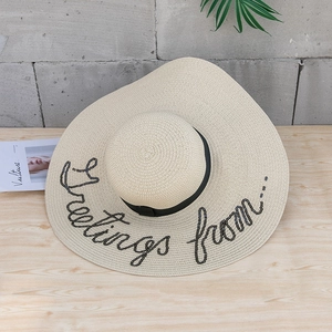 Détail d'un chapeau de paille beige avec ruban noir et broderie lettrée en paillettes