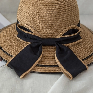 Close-up of a natural straw sun hat featuring a large black bow with woven texture edges