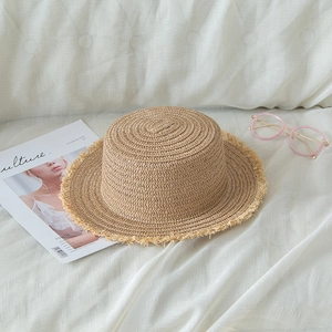 Close-up of flat-top straw boater hat with frayed edges next to a fashion magazine