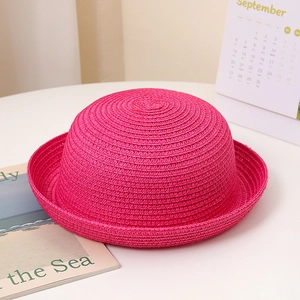 Détail d'un chapeau de soleil rose en paille tressée avec bord incurvé sur fond blanc