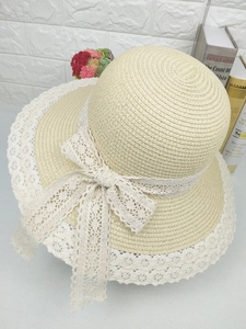 Détail du chapeau en paille crème avec un large nœud en dentelle et bordure en dentelle