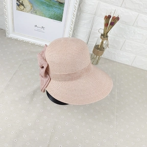Pink straw sun hat with large bow decoration on floral table in a pastoral setting