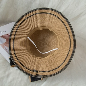 Detail of woven straw sun hat featuring black bow and interior windproof strap