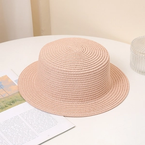 Close-up of pink straw boater hat with fine woven texture on white table background
