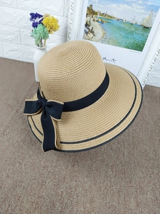 Detail view of woven straw hat featuring black bow ribbon and double stripe brim accents