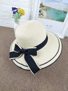 Detail of elegant cream straw sun hat featuring a large brim and black bow ribbon