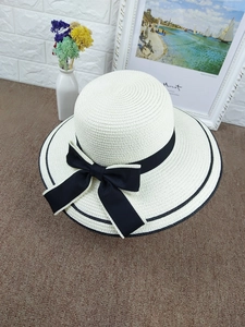 Top view of a white straw sun hat with black ribbon bow and elegant spiral weave detail