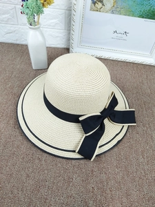 Detail of a beige woven straw hat featuring a wide brim and large black decorative bow
