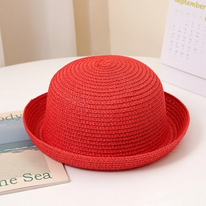 Détail d'un chapeau de soleil en paille rouge vif avec bord roulé sur un bureau blanc épuré