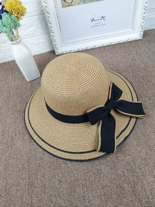 Top view of a wide brim straw hat with black ribbon bow on a cozy beige carpet
