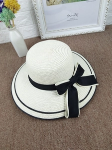 Detail view of the wide-brim straw hat featuring black stripes and a large side bow