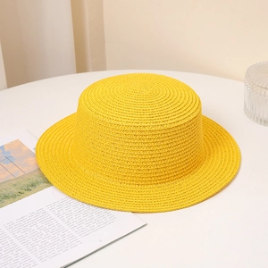 Summer bright yellow flat top boater straw hat for sun protection on a white table