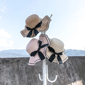 Three straw hats with wavy brims and black ribbon bows hanging on a white rack