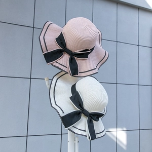 Detail of wide brim straw sun hats with black bow ribbon and scalloped edges