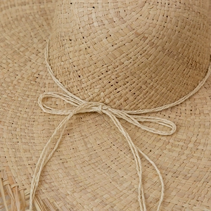 Detailed close-up of raffia sun hat texture with hand-woven rope bow and frayed edge