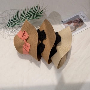 Close-up of three woven straw sun hats with elegant bow ribbons on a textured cloth