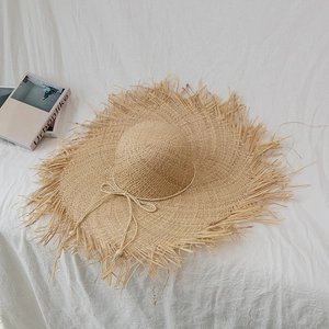 Top view of raffia sun hat with raw edges and beaded rope on white fabric