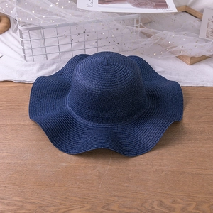 Navy blue wide brim floppy straw hat with wavy edges for sun protection on a wooden table