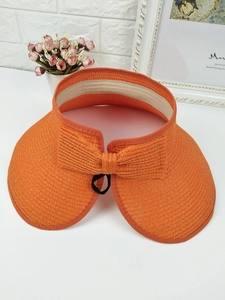 Detail of orange woven sun visor with straw texture and decorative bow on a white desk