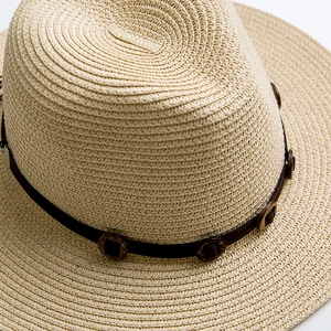 Dettaglio di un cappello di paglia con fascia in pelle marrone e bottoni in legno naturali