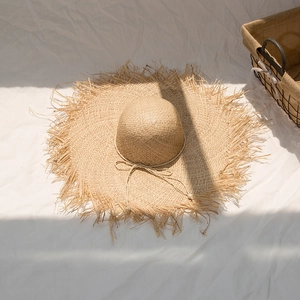 Detailed close-up of natural raffia straw sun hat with raw edge and beaded cord detail
