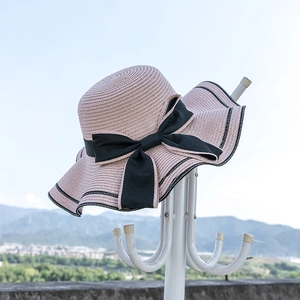 Women's pink wide brim straw sun hat with black ribbon bow and wavy edges for beach wear