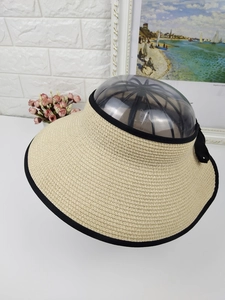 Detailed texture of beige straw sun visor with black ribbon trim and bow accent