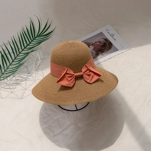 Women's summer straw sun hat with wide coral pink ribbon bow on display stand