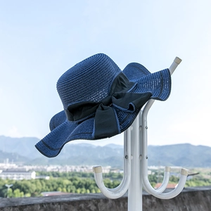 Navy blue woven straw sun hat with large black bow tie hanging on a white rack