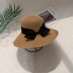Straw sun hat with wide brim and black bow ribbon decoration on white fabric background