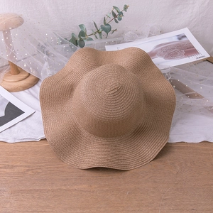 Detailed top view of a brown straw sun hat with wavy brim on a wooden surface