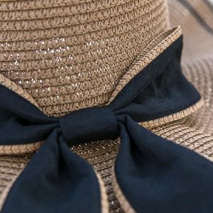 Detail of hand-woven straw sun hat with large black bow tie and scalloped edges