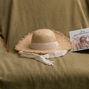 Detail of raffia sun hat with scalloped edges and white crochet lace ribbon on olive fabric
