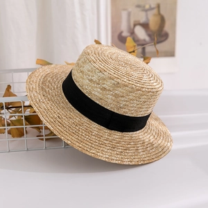 Detail of high-quality woven straw boater hat with a wide black ribbon on a white basket