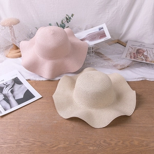 Detail of pink and beige wide-brim straw hats with wavy edges on a wooden table