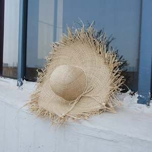 Detail of hand-woven raffia sun hat with frayed brim and adjustable chin strap
