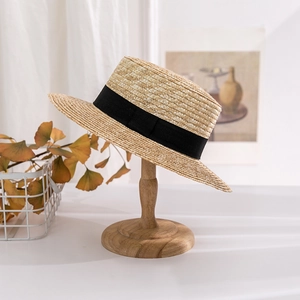 Detailed texture of a woven wheat straw boater hat with a black ribbon bow on a wooden stand