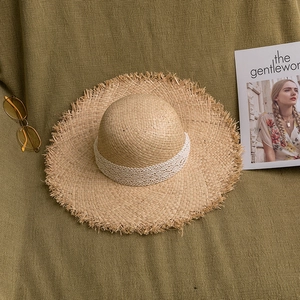 Detail of raffia straw hat with frayed edges and delicate white lace ribbon decoration